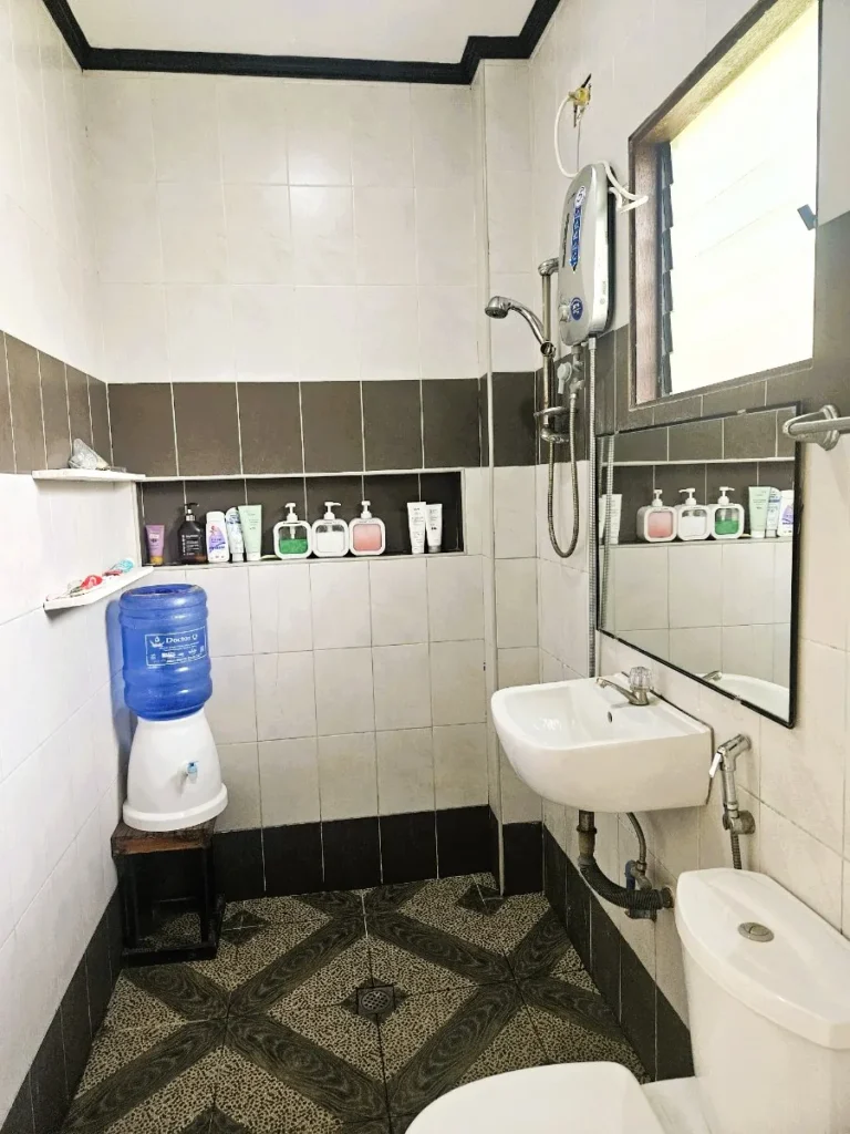 필리핀 세부 JJES 어학원 가족형 기숙사 화장실로, 온수기 샤워기와 세면대 옆에 파란 생수통 정수기가 놓여 있습니다.
