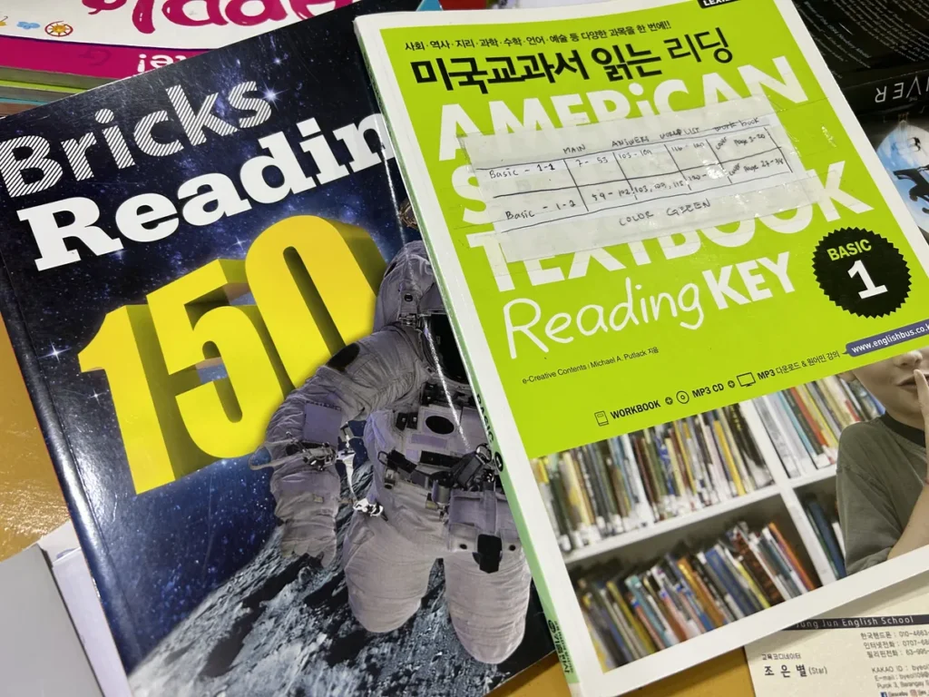 필리핀 세부 JJES 어학원 강의실 교재로, Bricks Reading 150과 미국교과서 리딩 Basic 1 교재가 겹쳐 쌓인 리딩 학습서 모습입니다.