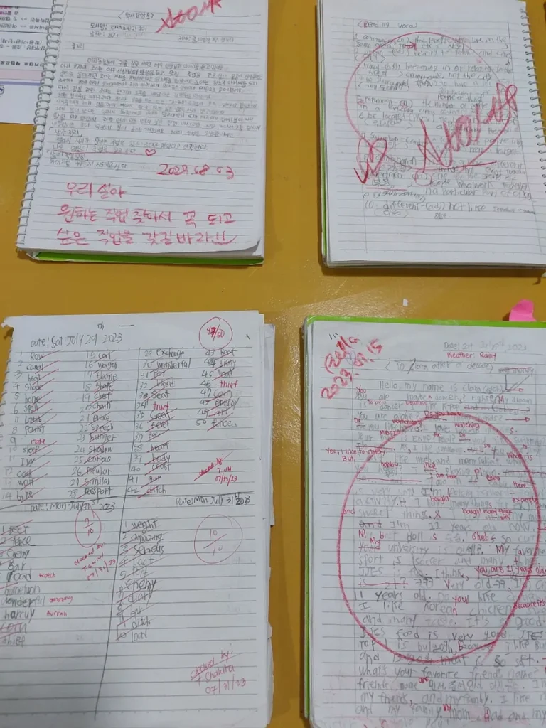 필리핀 세부 JJES 어학원 강의실 교재로, 단어 뜻풀이와 스펠링 시험지, 학생이 손으로 쓴 편지가 펼쳐진 개인 학습 노트 네 권입니다.