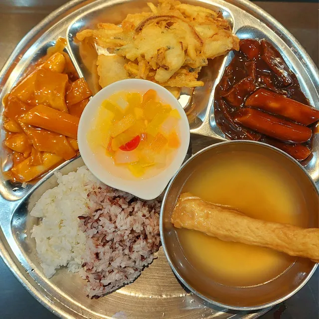 필리핀 세부 JJES 어학원 학생식당 식사로, 매콤달콤 야채볶음과 부추전·간장소세지에 과일, 잡곡밥과 계란국을 곁들인 식판입니다.