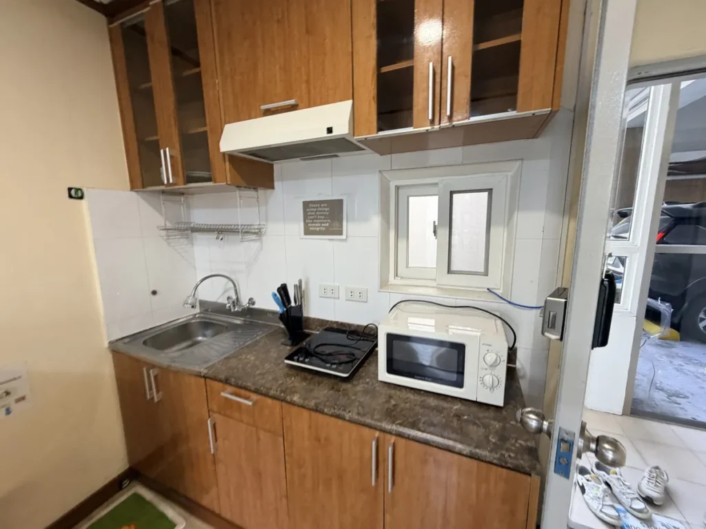 필리핀 바기오 웨일즈(WALES) 어학원 기숙사 P스튜디오 주방으로, 스테인리스 개수대와 인덕션·전자레인지가 놓인 목재 조리대가 보이는 공간입니다.