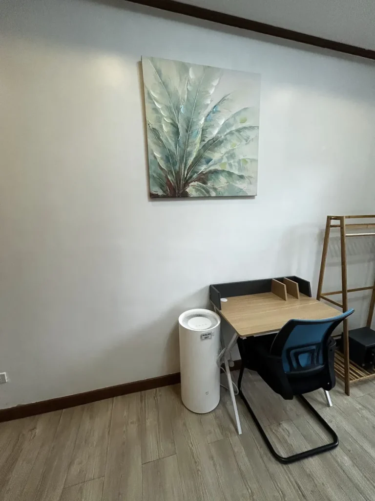 필리핀 바기오 웨일즈(WALES) 어학원 기숙사 1인실 스튜디오(2인가족)로, 그림 액자 아래 책상과 공기청정기가 놓인 학습 공간입니다.