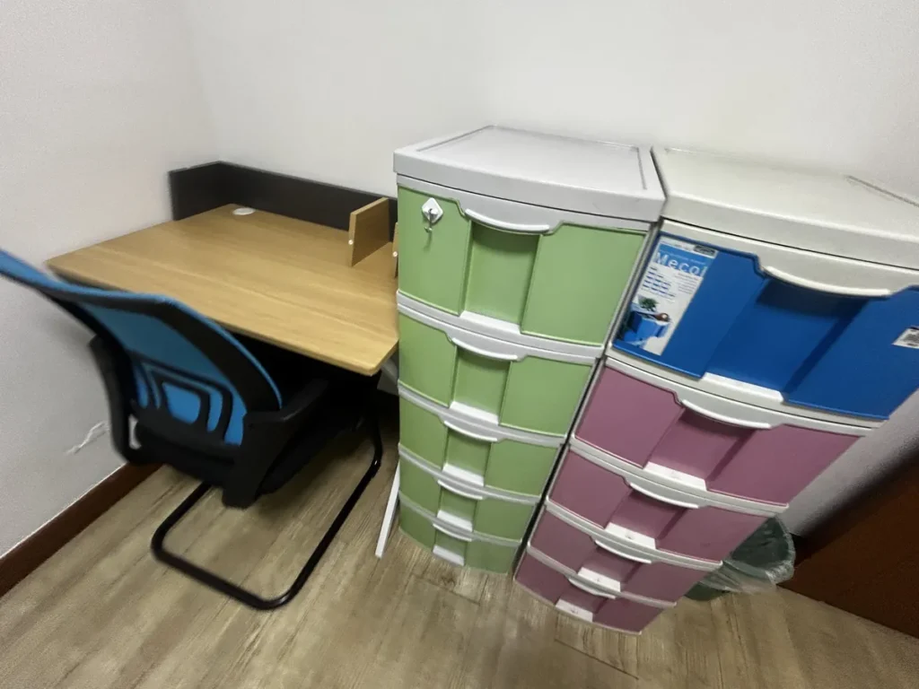 필리핀 바기오 웨일즈(WALES) 어학원 기숙사 1인실 공유형으로, 책상과 의자 옆에 초록·보라색 3단 서랍장 두 개가 나란히 놓인 수납 공간입니다.