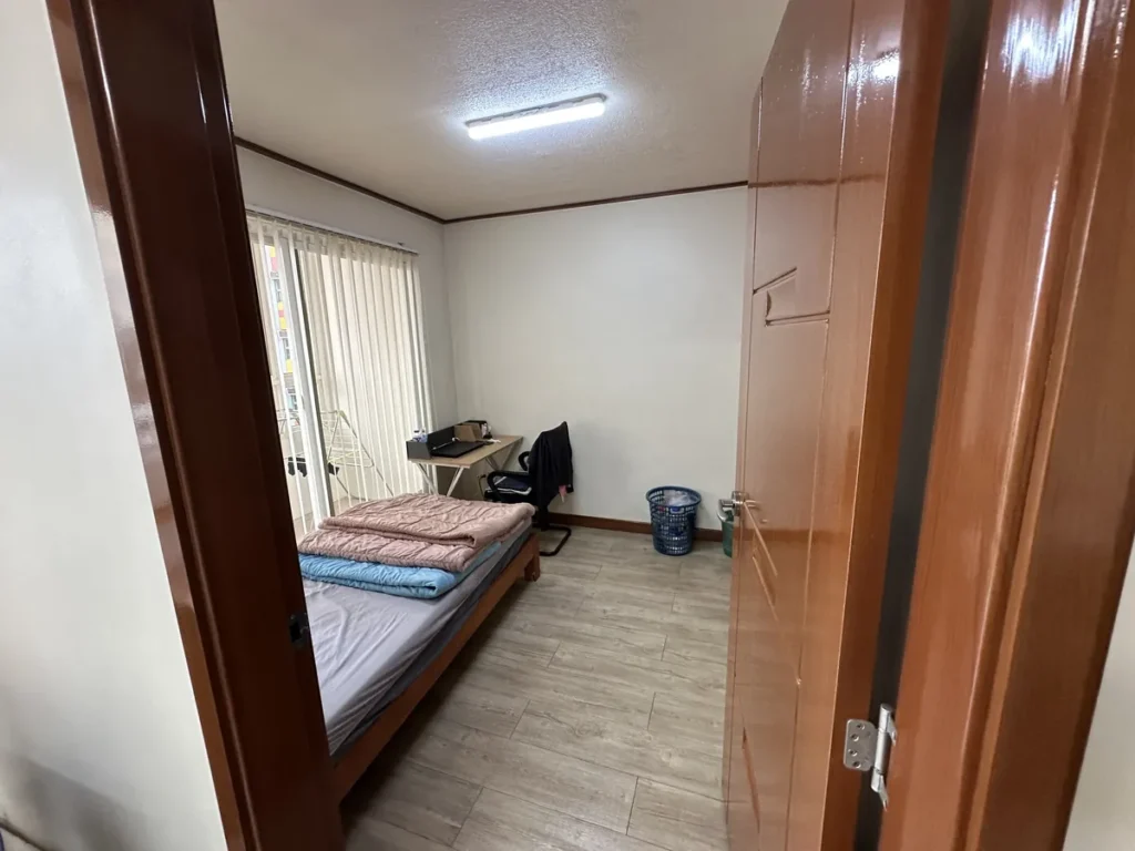 필리핀 바기오 웨일즈(WALES) 어학원 기숙사 1인실 공유형(베란다)로, 침대와 책상·의자, 세로 블라인드가 있는 방입니다.