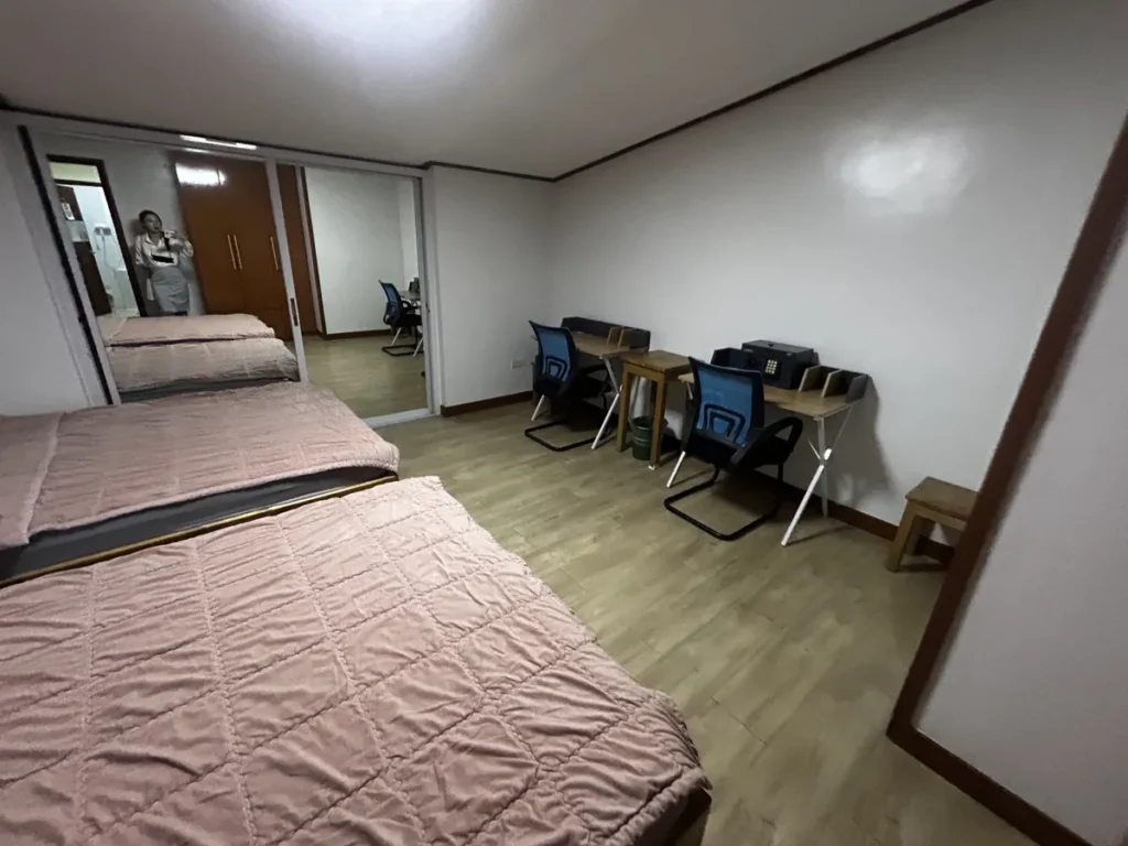 필리핀 바기오 웨일즈(WALES) 어학원 기숙사 2인실 공유형으로, 침대 옆 책상 두 개와 개인 금고, 거울 속 옷장이 있는 공간입니다.