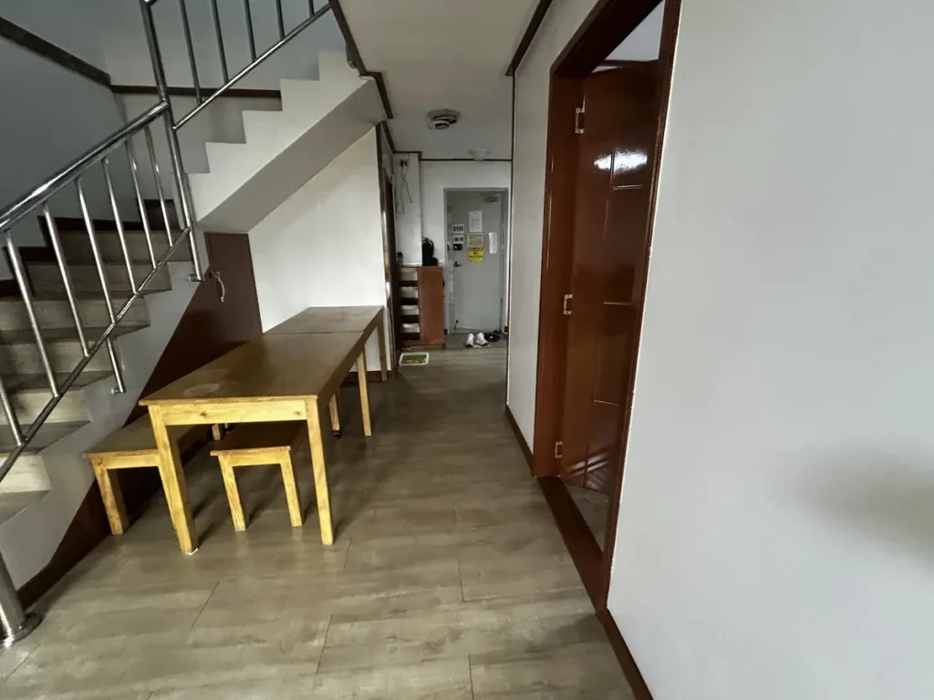 필리핀 바기오 웨일즈(WALES) 어학원 기숙사 공유형 공용공간으로, 계단 아래 원목 테이블과 벤치를 놓은 공용 취식 공간입니다.