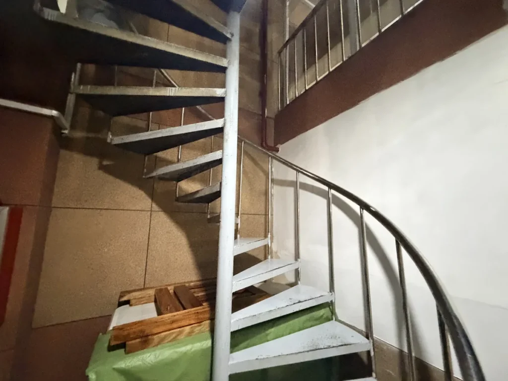 필리핀 바기오 웨일즈(WALES) 어학원 부대시설 휴게공간으로, 흰색 철제 난간의 나선형 계단이 위층으로 이어지는 모습입니다.