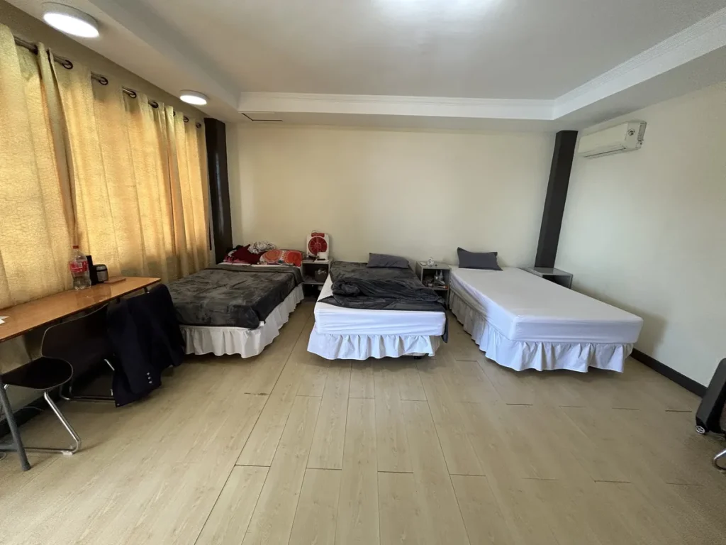 필리핀 세부 CIJ 어학원 3인실로, 노란 커튼 창가 쪽 책상과 흰 시트의 침대 세 개, 협탁과 벽걸이 에어컨이 있는 객실입니다.