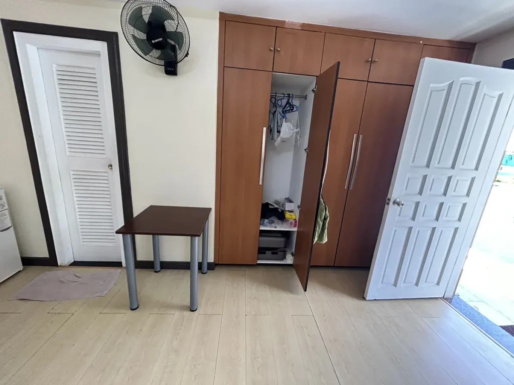 필리핀 세부 CIJ 어학원 3인실로, 한 칸이 열린 원목 옷장과 작은 테이블, 벽걸이 선풍기와 화장실 문이 보이는 객실 입구 쪽입니다.