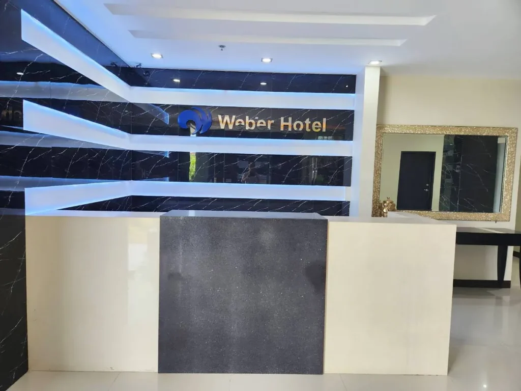 필리핀 세부 CIJ 어학원 외부숙소 로비로, 검은 대리석 벽에 Weber Hotel 간판과 조명이 들어간 프런트 데스크와 금색 액자 거울입니다.