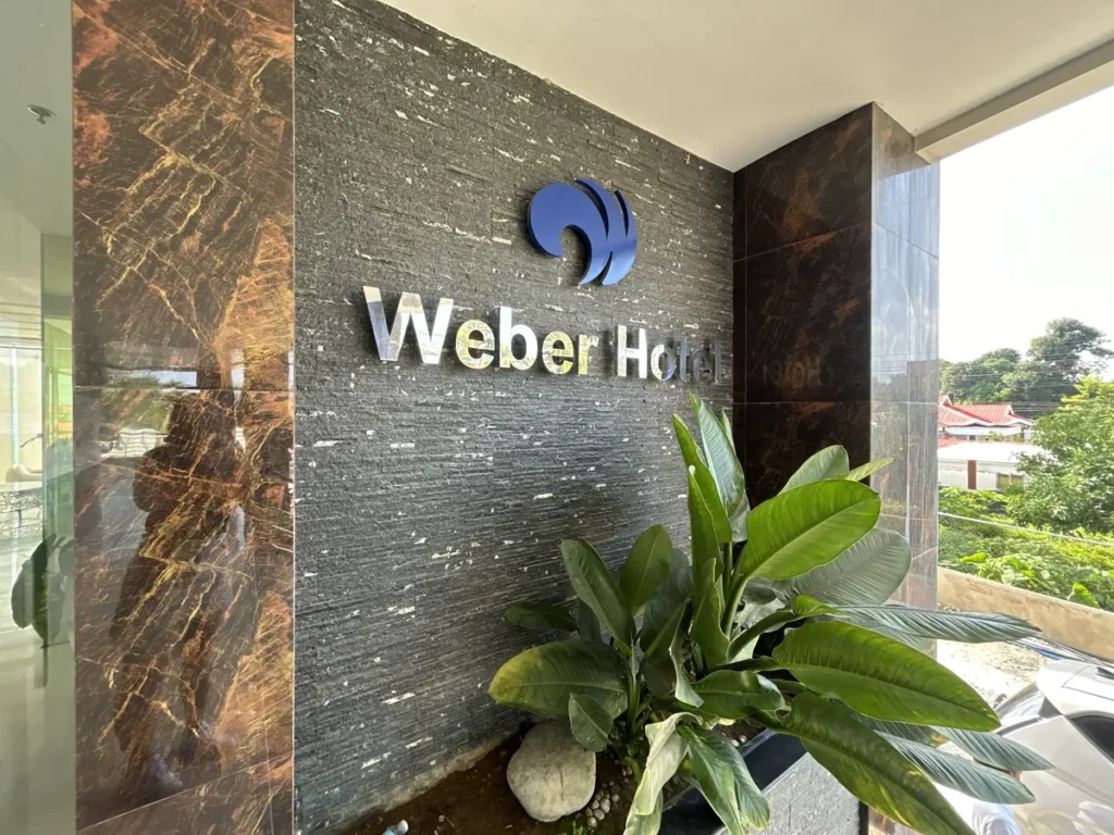 필리핀 세부 CIJ 어학원 외부숙소 외관으로, 석재 벽면의 Weber Hotel 로고 간판과 큰 잎 관엽식물 화단이 있는 입구 옆 모습입니다.