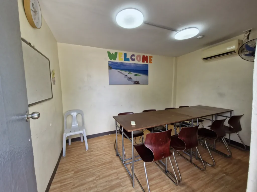 필리핀 세부 CIJ 어학원 그룹 강의실로, WELCOME 문구와 바다 그림 아래 긴 테이블과 의자 여러 개를 둔 교실입니다.
