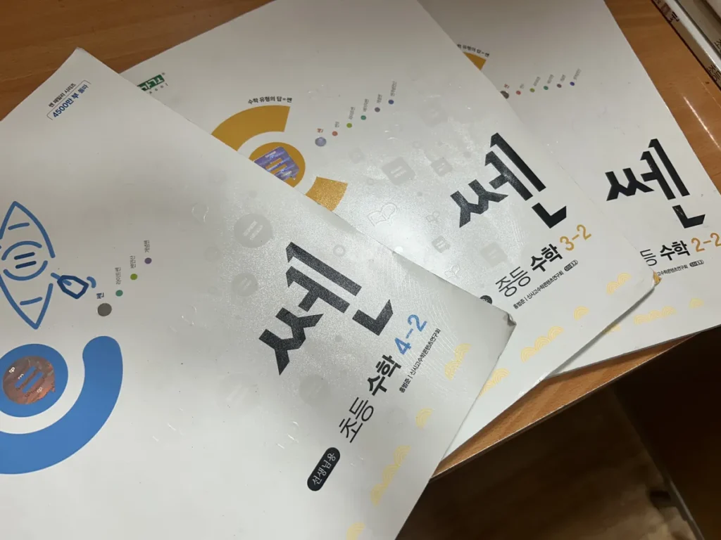 필리핀 세부 CIJ 어학원 교재로, 책상 위에 초등 수학 4-2와 중등 수학 3-2·2-2 쎈 문제집이 겹쳐 놓여 있는 모습입니다.