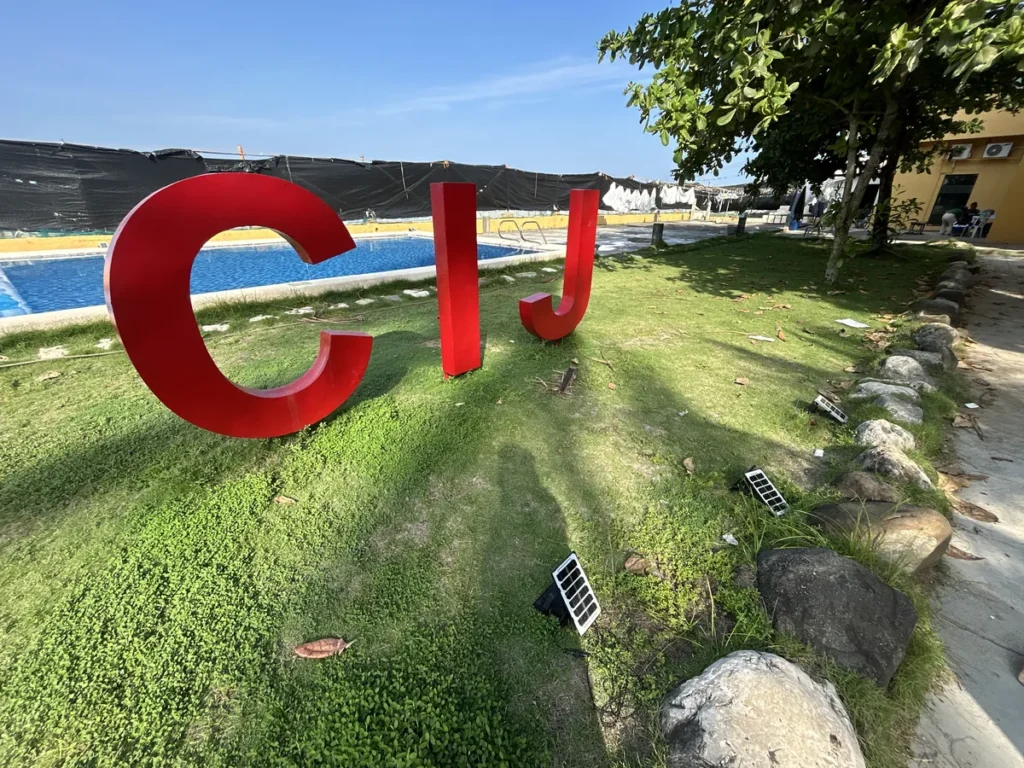 필리핀 세부 CIJ 어학원 수영장으로, 잔디밭에 세워진 빨간 CIJ 대형 글자와 태양광 정원등, 뒤편 직사각형 풀이 가까이 보이는 장면입니다.