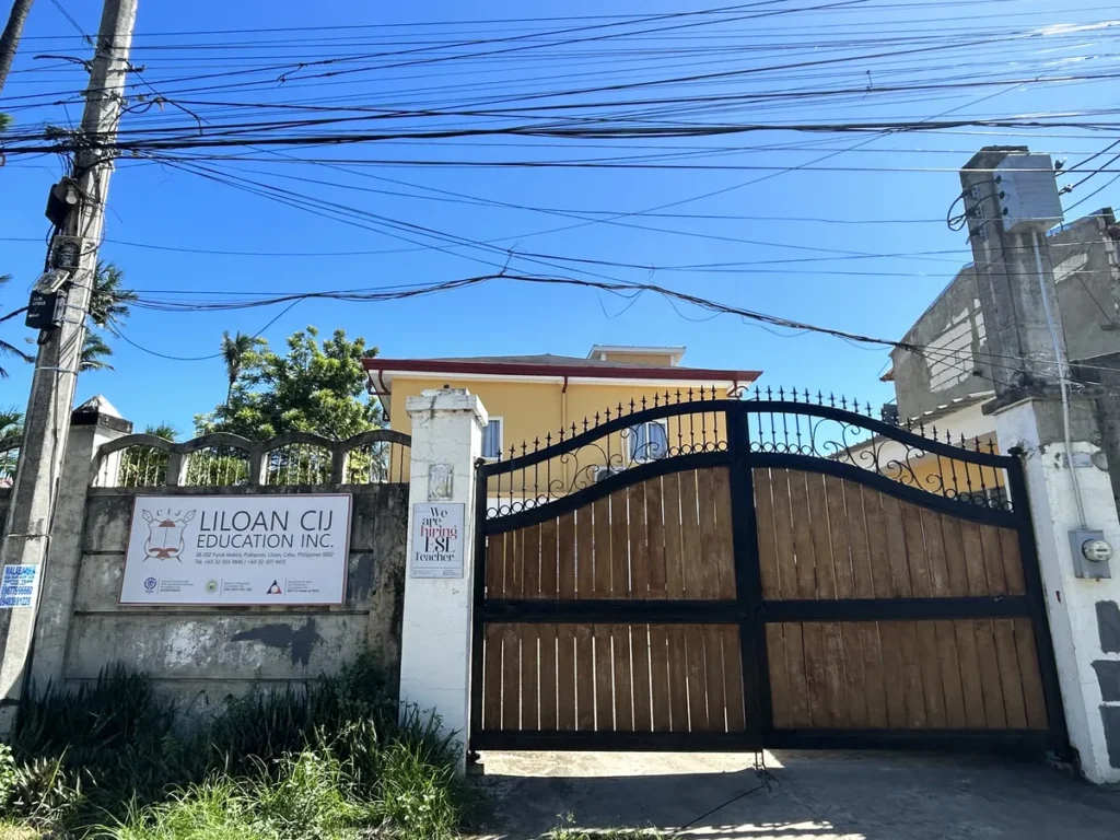 필리핀 세부 CIJ 어학원 입구로, LILOAN CIJ EDUCATION 간판이 걸린 담장과 원목 철제 대문 너머 노란 외벽 건물이 보이는 모습입니다.