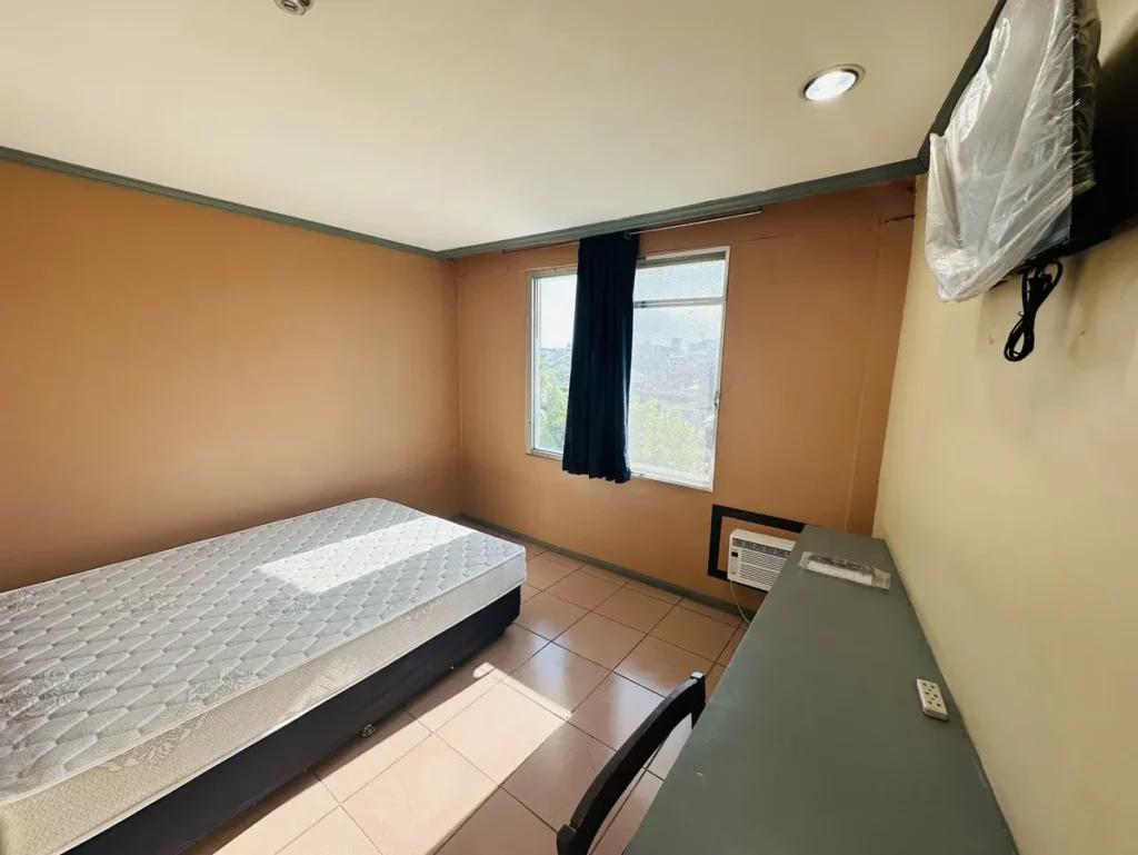필리핀 세부 시필스(CPILS) 어학원 기숙사 1인실(프리미엄룸)으로, 창가 쪽 싱글 침대와 벽면 책상, 창문형 에어컨이 놓인 방입니다.
