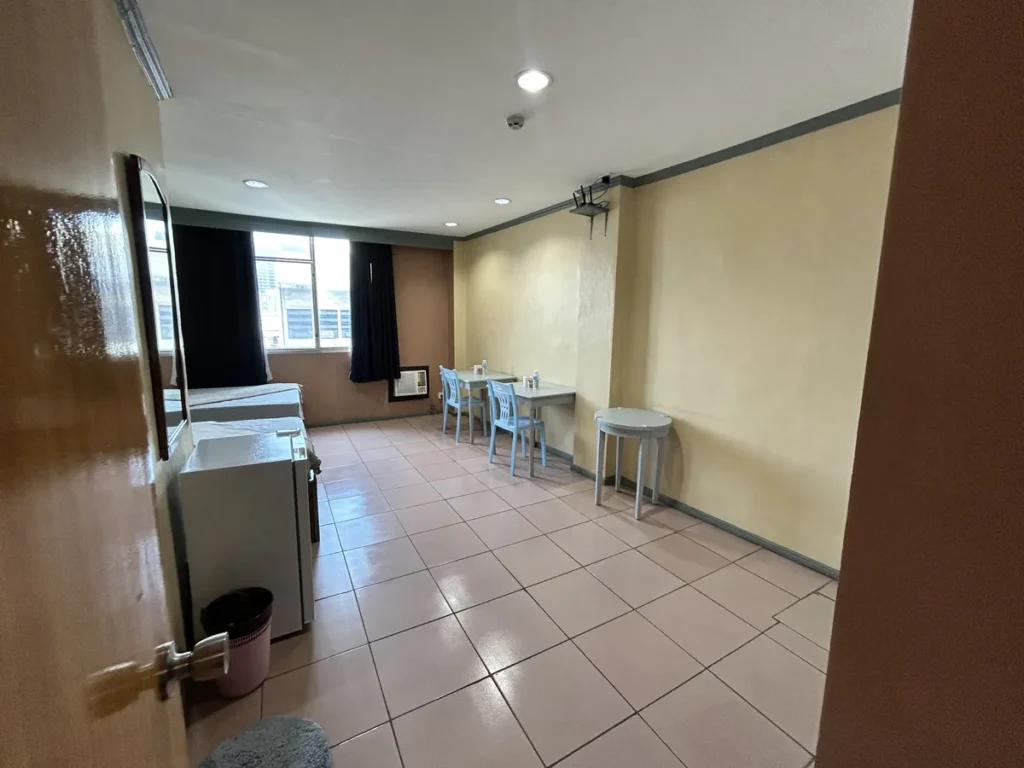 필리핀 세부 시필스(CPILS) 어학원 기숙사 2인실로, 출입문에서 바라본 긴 객실에 책상 두 개와 원형 보조 테이블이 벽을 따라 놓인 모습입니다.
