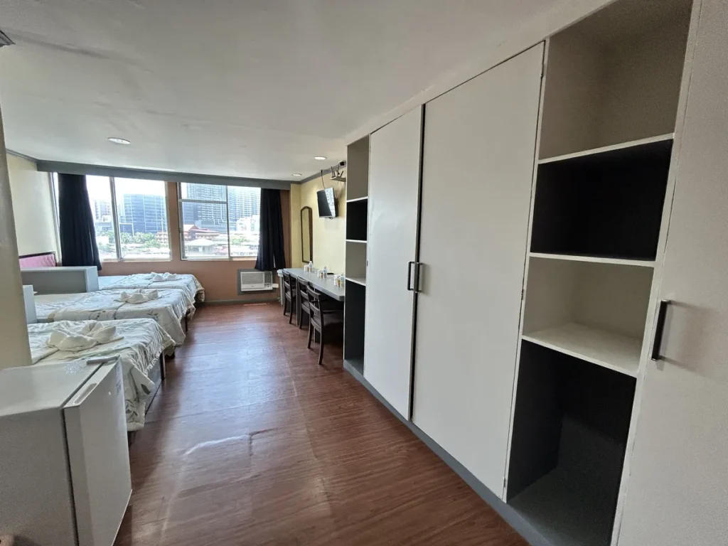 필리핀 세부 시필스(CPILS) 어학원 기숙사 3인실 프리미엄룸으로, 오른쪽 벽면의 붙박이 옷장과 선반 너머로 침대와 책상이 이어지는 모습입니다.