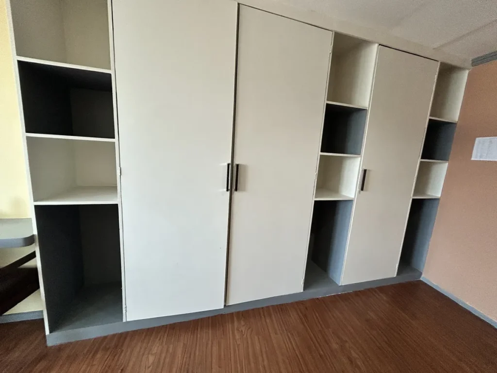 필리핀 세부 시필스(CPILS) 어학원 기숙사 3인실 프리미엄룸으로, 여닫이 문 3칸과 칸칸이 열린 선반이 이어진 흰색 붙박이 옷장입니다.