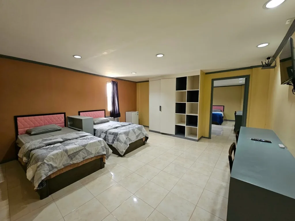 필리핀 세부 시필스(CPILS) 어학원 기숙사 4인실(일반룸)으로, 분홍 헤드보드 침대 두 대와 수납장·벽걸이 TV가 놓인 넓은 방입니다.