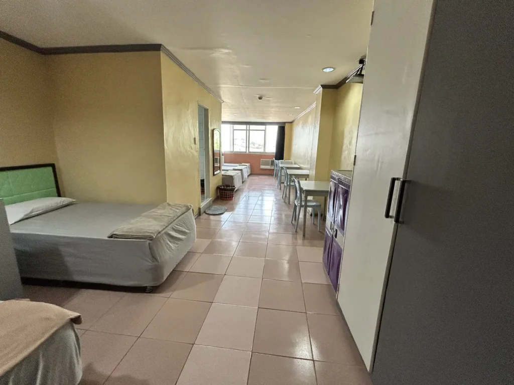 필리핀 세부 시필스(CPILS) 어학원 기숙사 5인실 일반룸으로, 길게 이어진 타일 바닥 객실에 싱글침대와 책상·의자, 수납장이 놓인 모습입니다.