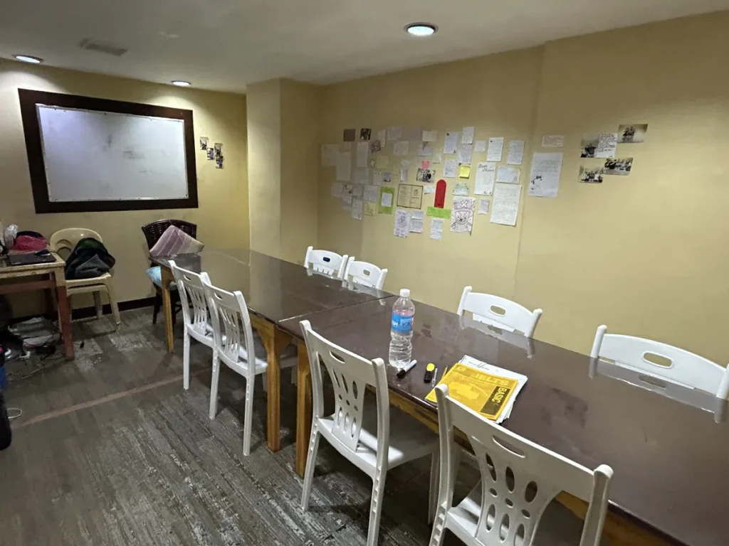 필리핀 세부 시필스(CPILS) 어학원 그룹 강의실로, 화이트보드와 학생 메모가 붙은 벽 앞에 긴 테이블 두 개가 이어진 교실입니다.