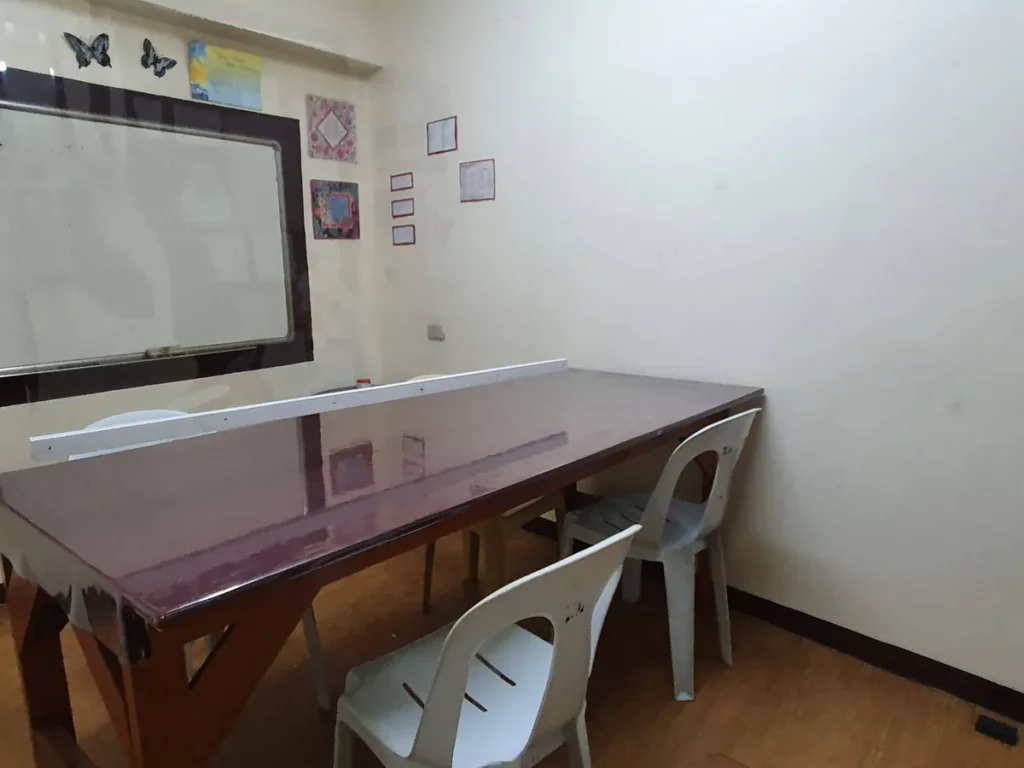 필리핀 세부 시필스(CPILS) 어학원 그룹 강의실로, 칸막이가 놓인 긴 테이블과 흰 플라스틱 의자, 원목 바닥이 보이는 교실입니다.