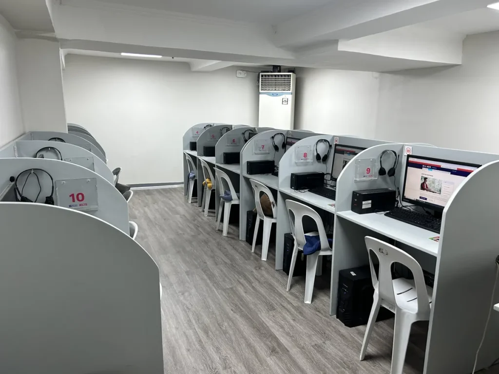 필리핀 세부 시필스(CPILS) 어학원 아이엘츠 시험장으로, 번호가 붙은 칸막이 부스마다 모니터·헤드셋·키보드가 갖춰진 컴퓨터 시험실입니다.