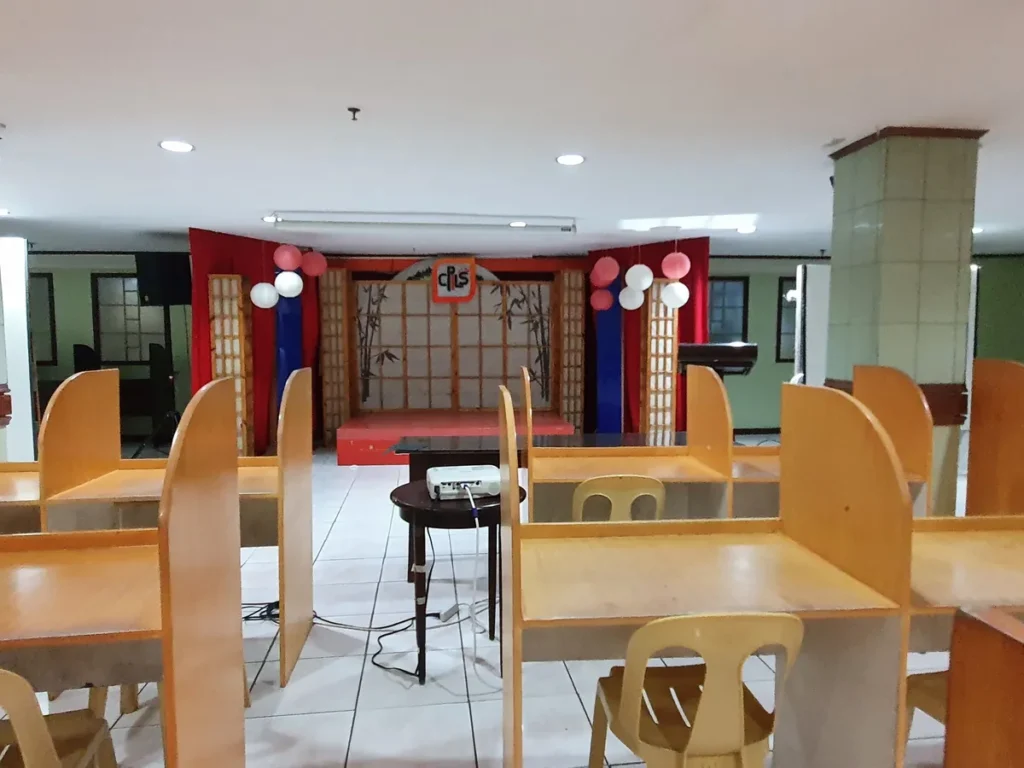 필리핀 세부 시필스(CPILS) 어학원 토익시험장으로, CPILS 로고와 대나무 그림 장식이 있는 무대 앞에 프로젝터가 놓인 모습입니다.