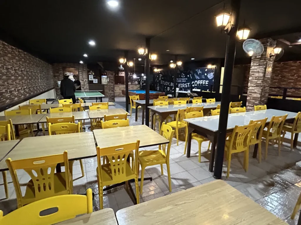 필리핀 세부 시필스(CPILS) 어학원 휴게공간으로, 노란 의자와 테이블이 줄지어 있고 안쪽에 탁구대와 당구대가 보이는 카페형 공간입니다.