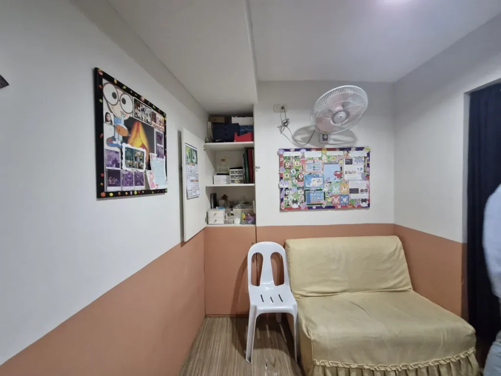 필리핀 세부 시필스(CPILS) 어학원 클리닉으로, 게시판과 벽걸이 선풍기 아래 소파와 의자, 비품 선반이 놓인 대기 공간입니다.