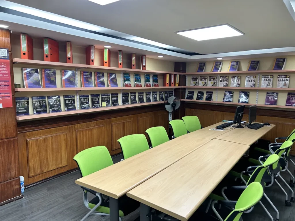 필리핀 세부 시필스(CPILS) 어학원 아이엘츠자료실로, 벽면 선반 가득 IELTS 교재가 진열되고 연두색 의자와 긴 테이블이 놓인 학습공간입니다.