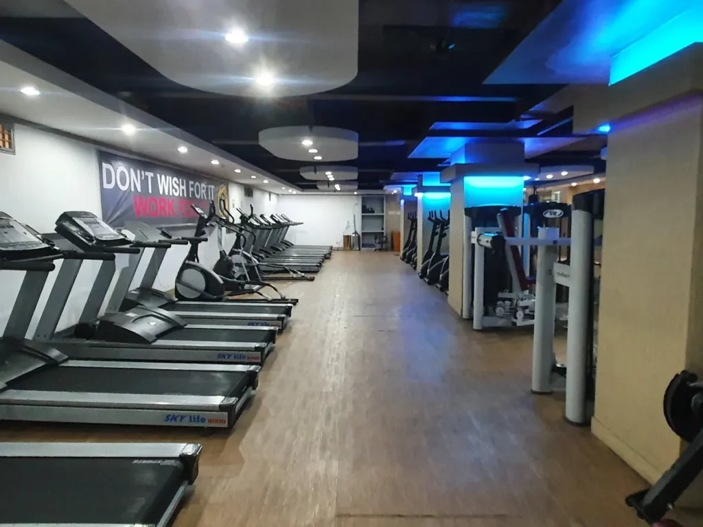 필리핀 세부 시필스(CPILS) 어학원 헬스장으로, 러닝머신과 일립티컬이 벽을 따라 한 줄로 놓이고 맞은편에 웨이트 머신이 있는 모습입니다.