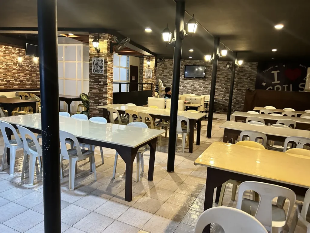 필리핀 세부 시필스(CPILS) 어학원 식당으로, 벽돌 무늬 벽과 랜턴 조명 아래 테이블과 소파 좌석이 놓인 카페형 공간입니다.