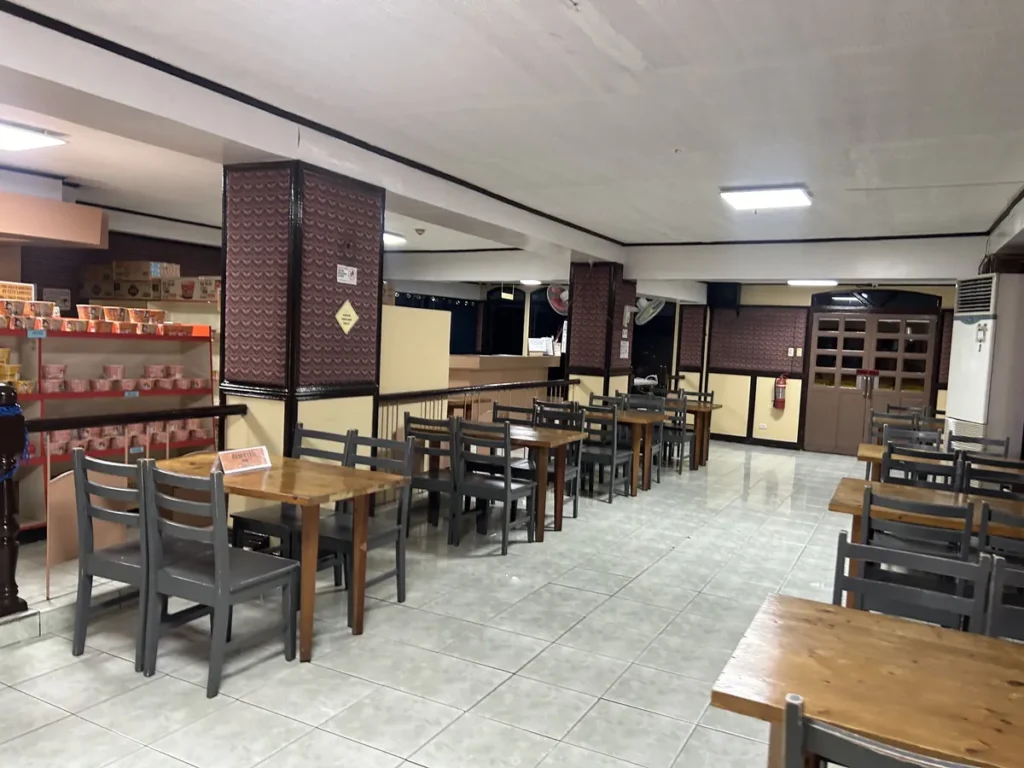 필리핀 세부 시필스(CPILS) 어학원 식당으로, 원목 테이블 좌석 옆으로 컵라면이 진열된 매점 선반이 함께 보이는 공간입니다.
