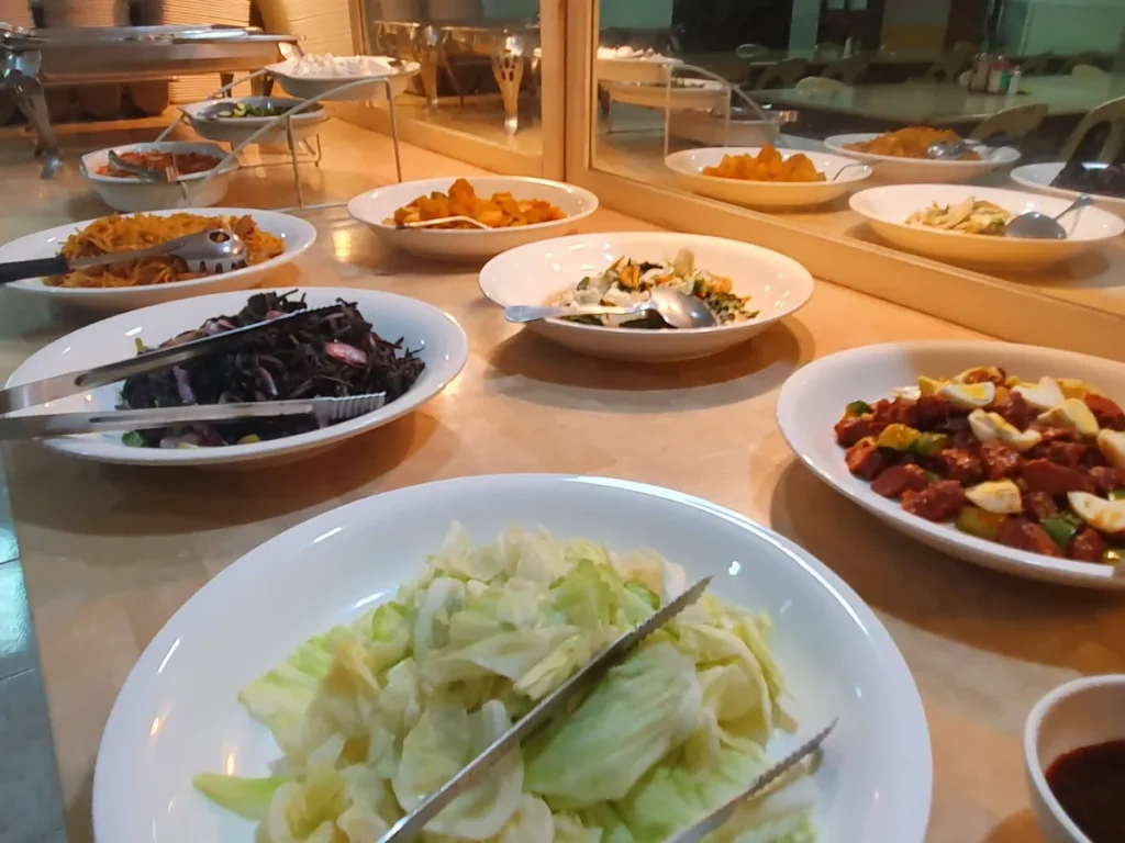 필리핀 세부 시필스(CPILS) 어학원 식당 식사 메뉴로, 양배추·적양배추무침·볶음국수·단호박조림이 흰 접시에 줄지어 놓인 반찬 배식대입니다.