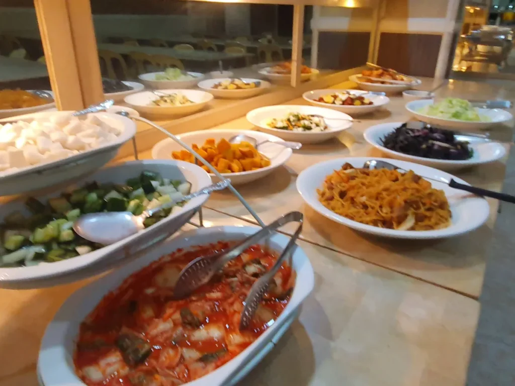 필리핀 세부 시필스(CPILS) 어학원 식당 식사 메뉴로, 김치·깍두기·오이무침 같은 한식 반찬과 볶음국수가 함께 차려진 배식대입니다.