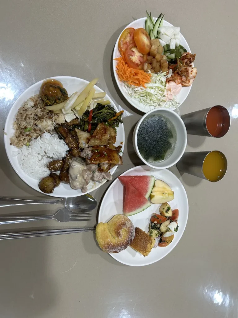 필리핀 세부 시필스(CPILS) 어학원 식당 식사 메뉴로, 위에서 본 쌀밥·볶음밥·고기반찬 접시와 김치 샐러드·미역국·수박·빵·주스 구성입니다.
