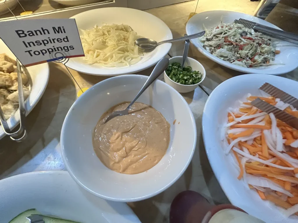 필리핀 세부 시필스(CPILS) 어학원 식당 식사 메뉴로, Banh Mi 안내판 옆에 당근무 절임·소스·청고추·양배추무침을 차린 반미 토핑 코너입니다.